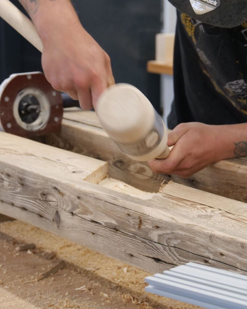 Handwerksszene mit Holzarbeiten, ein Arbeiter schlägt mit Holzhammer auf Balken.